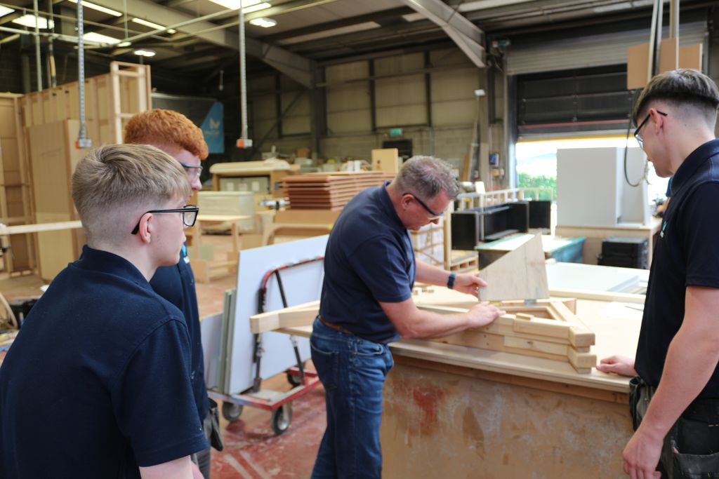 McCue joiner guiding three apprentices through a timber frame on the workshop floor
