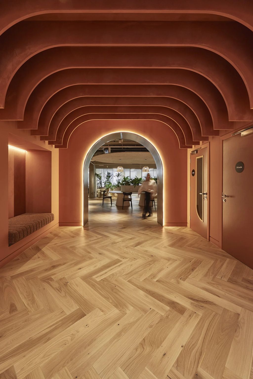 Mountbatten House: terracotta arched corridor with stepped ceiling ribs and a glowing steel-framed archway onto oak herringbone floor