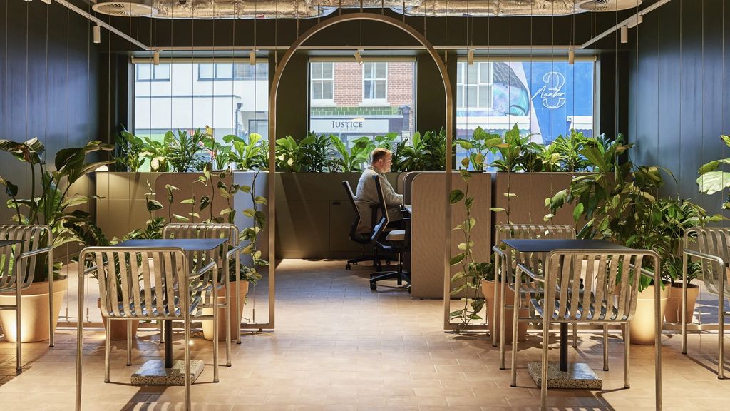 Mountbatten House: planted café and focus area framed by a slim metal arch, with galvanised chairs and street views