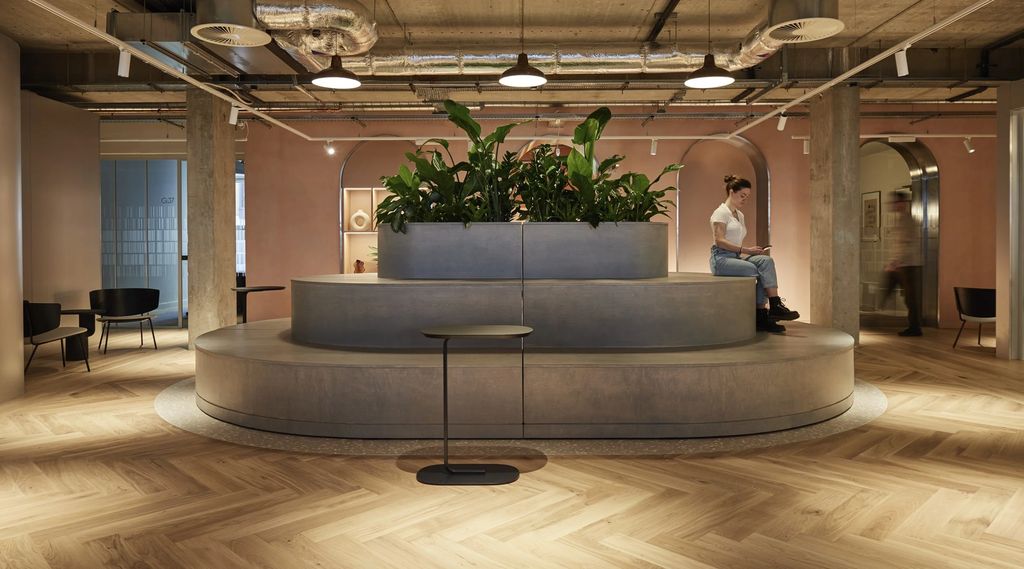 Mountbatten House: tiered oval seating planter in grey timber on herringbone oak, beneath exposed services